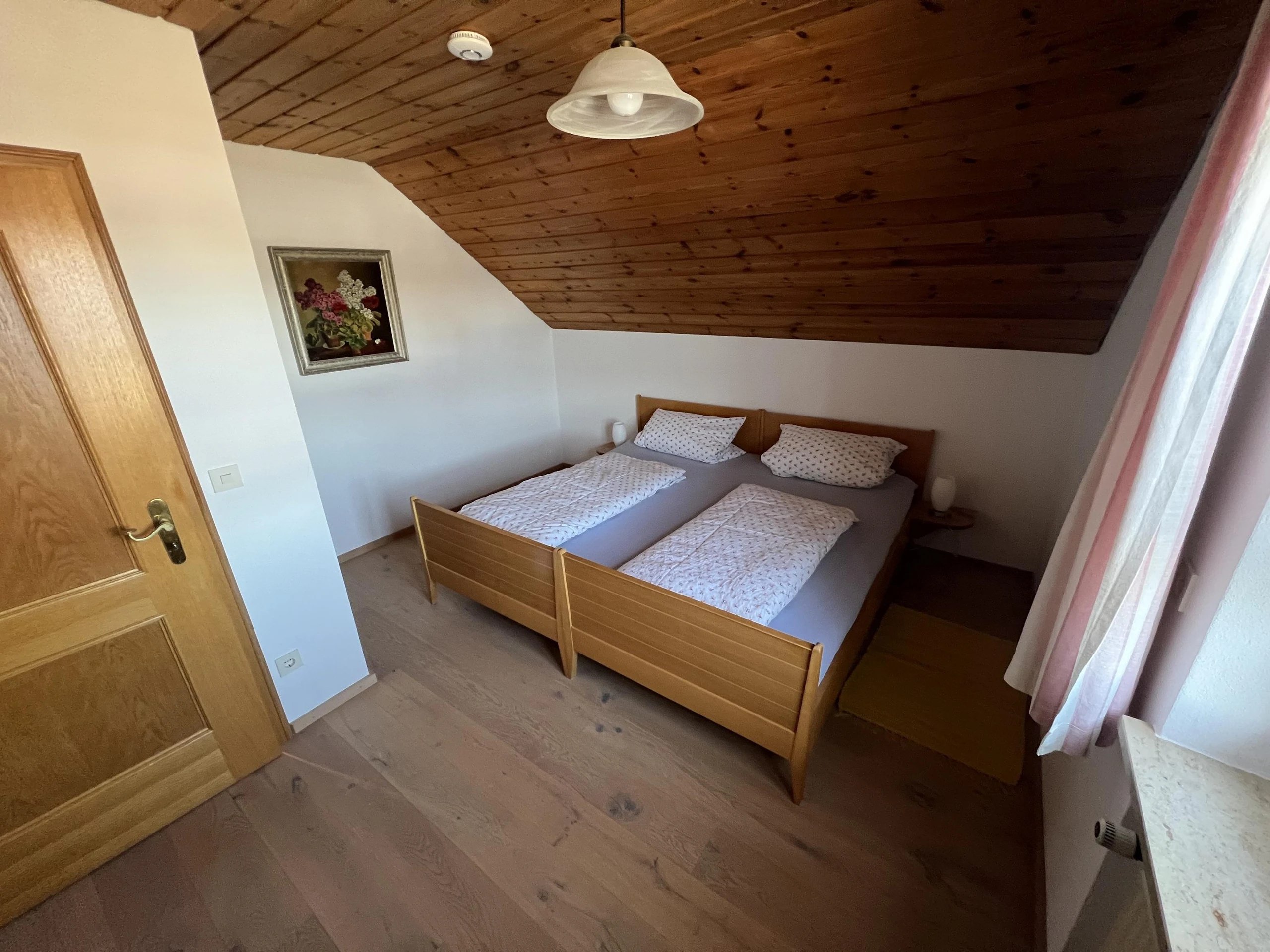 Schlafzimmer mit Doppelbett, warmer Holzdecke, hellen Wänden und ruhiger bayerischer Atmosphäre