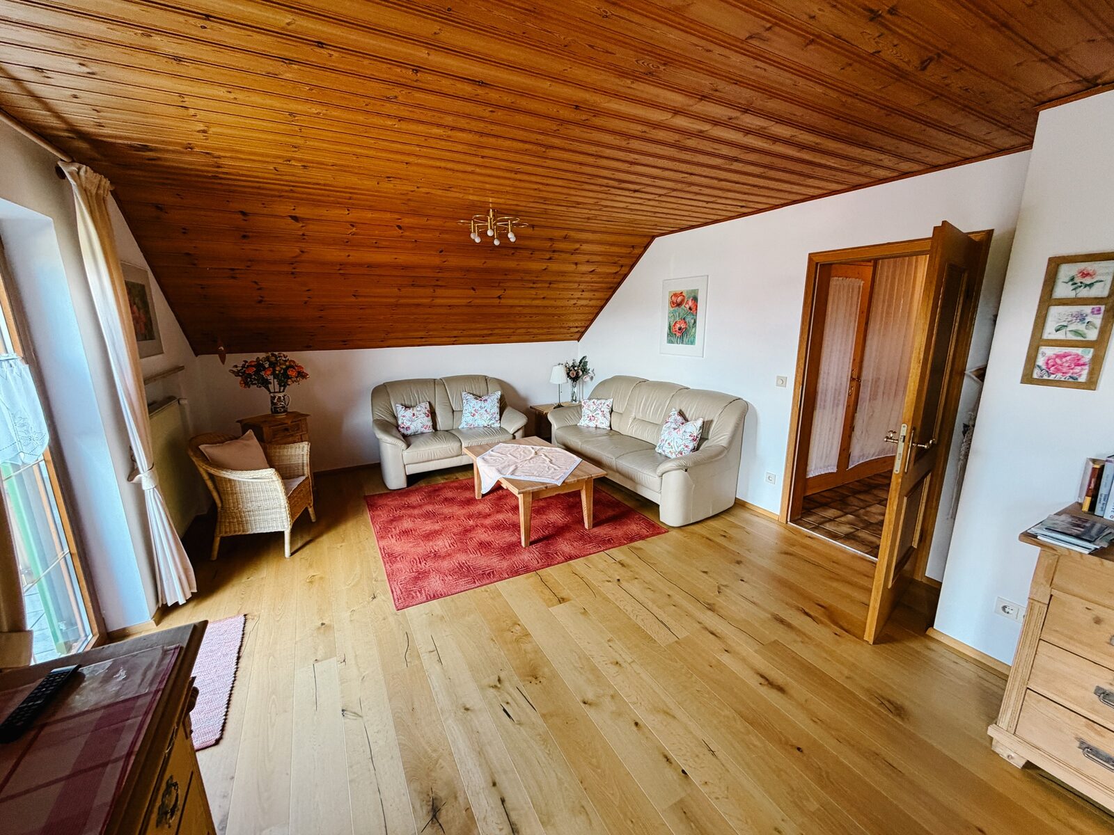 Wohnbereich mit gemütlicher Sitzecke, Holzdecke, Teppich und heller Atmosphäre unter dem Dach